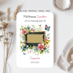 Peut inclure: Une carte blanche avec des illustrations florales et de papillons. La carte contient du texte en français, dont "Maîtresse Caroline" et "J'ai un message pour toi." Un espace rectangulaire est au centre. La carte comprend également le nom "Capucine" et les années "2025-2026."
