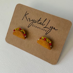 May include: A pair of small, handmade taco earrings. The earrings are made of polymer clay and are painted to look like real tacos. The tacos are filled with ground beef, lettuce, cheese, and tomatoes.