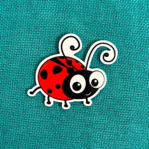 Puede incluir: Una pegatina de mariquita roja y negra con un contorno blanco. La mariquita tiene manchas negras en la espalda y ojos grandes de dibujos animados. La pegatina está sobre un fondo turquesa.
