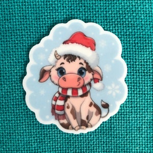 May include: A cartoon cow wearing a red Santa hat and a red and white striped scarf. The cow is sitting on a blue background with snowflakes.
