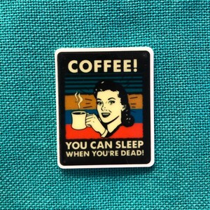 May include: A white sticker with a retro-style illustration of a woman drinking coffee. The text on the sticker reads "COFFEE! YOU CAN SLEEP WHEN YOU'RE DEAD!"
