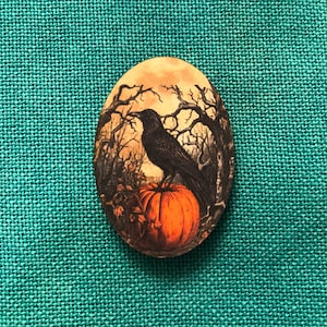 May include: Oval-shaped wooden Halloween decoration featuring a black crow perched on an orange pumpkin. The background depicts a spooky forest scene with bare trees under a cloudy sky. The decoration is set against a textured teal background.