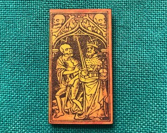 May include: A vintage-style illustration of a skeleton holding a sword and standing next to a crowned figure. The image is printed on a rectangular wooden plaque with a yellow and orange gradient.