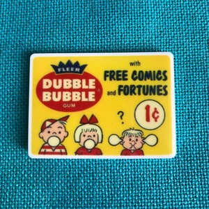 May include: A vintage yellow and red Dubble Bubble gum wrapper with a crown logo. The wrapper features three children blowing bubbles and the text "with FREE COMICS and FORTUNES 1¢".