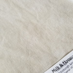 Puede incluir: Primer plano de un trozo de tela de lino beige. La tela tiene una textura tejida con hilos visibles. El color es un tono claro y neutro, adecuado para diversos proyectos de costura y artesanía. La tela es un cuarto de yarda.