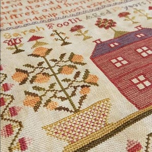 Puede incluir: Un sampler de punto de cruz con una casa roja, un naranjo en maceta y el texto "Sarah Footit" en un marco marrón.