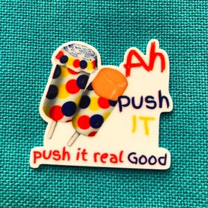 May include: A sticker featuring two push-up popsicles with white, red, yellow, and blue polka dots. The text reads Ah push IT push it real Good in red, blue, and yellow lettering. The design is on a white background with a die-cut edge.