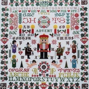 May include: A white cross-stitch sampler with a Christmas theme. It features a nutcracker, candles, ornaments, and the words "Advent" and "Anno 2000".
