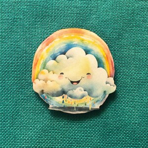 May include: A colourful pin badge depicting a smiling cloud with a rainbow above it. The cloud has a happy face and is surrounded by a rainbow. The pin is set against a teal green fabric background.
