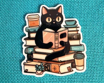 Könnte beinhalten: Ein Aufkleber mit einer schwarzen Katze, die ein Buch liest und auf einem Stapel Bücher sitzt. Die Katze hat große gelbe Augen und ist von Kaffeetassen und einer kleinen Topfpflanze umgeben. Der Aufkleber befindet sich auf einem türkisfarbenen Hintergrund.