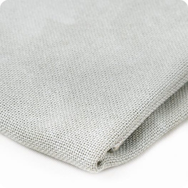 Puede incluir: Primer plano de una tela tejida de color gris claro. La tela tiene una textura sutil y un acabado liso.