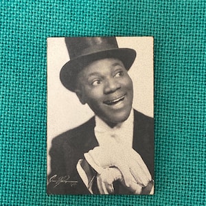 May include: Black and white photo of a man wearing a top hat and a suit. He is smiling and looking at the camera. The photo is signed with a name.