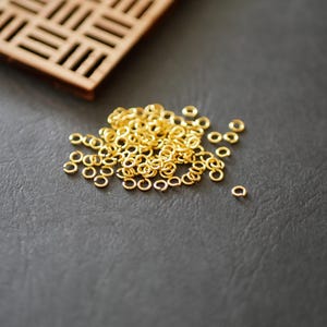 以下が含まれることがあります： 暗い灰色の表面に散らばる、小さな金色の丸カン。 格子模様の木製の長方形のオブジェクトが左上にあります。 丸カンは丸く、金属製のように見えます。