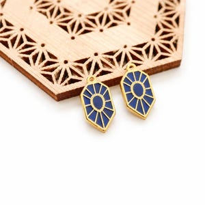 Peut inclure: Deux breloques en métal en forme de bouclier avec une bordure dorée et un ovale central entouré de lignes rayonnantes, le tout rempli d'émail bleu profond. Chaque breloque comprend une petite boucle circulaire au sommet pour la fixation.