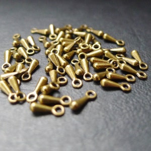May include: A pile of gold-toned metal teardrop-shaped charms with jump rings. The charms are approximately 2.5 cm long.