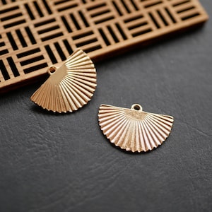 May include: Two gold-colored metal fan-shaped charms with a hole at the top for attaching to jewelry or other crafts.