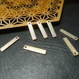 May include: A collection of eight gold-toned metal bar charms with a textured finish. The charms have a hole at each end for attaching to jewellery or other crafts.