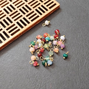 May include: Assortment of colourful gemstone beads with gold jump rings. The beads are in various shades of green, red, pink, and white.