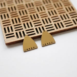 Peut inclure: Deux composants de boucles d'oreilles jaune moutarde en forme de triangle avec une base plate et un sommet arrondi. Chaque pièce présente un petit trou au sommet et une rangée de cinq petits trous espacés le long du bord inférieur.