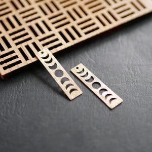K&ouml;nnte beinhalten: Zwei Holzohrringe mit einem Halbmond-Design. Die Ohrringe sind aus Holz ausgeschnitten und haben eine nat&uuml;rliche Holzoptik.