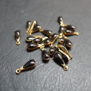 Peut inclure: Un groupe de perles de verre noires en forme de goutte avec des accents en métal doré. Les perles sont éparpillées sur une surface gris foncé.