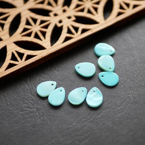 May include: A collection of seven light blue, teardrop-shaped, shell-like beads with a small hole at the top.