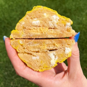 May include: A yellow cookie with a white and yellow filling, cut in half and held in a hand.