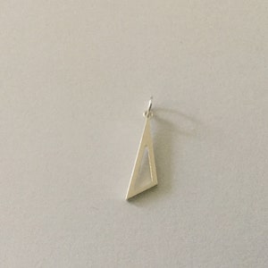 Pode incluir: Um pingente de triângulo de prata com um design recortado. O pingente tem um laço na parte superior para prender a uma corrente.