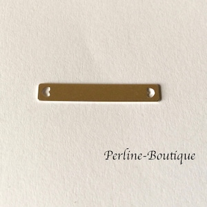 Peut inclure: Une barre en métal de couleur dorée avec deux découpes en forme de cœur. La barre est plate et rectangulaire.