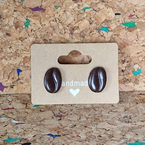 May include: A pair of brown coffee bean stud earrings on a card with the word "handmade" printed on it.