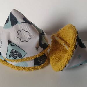 Peut inclure: Deux bavoirs pour bébé en forme de cône avec une bordure jaune. Un bavoir est blanc avec un motif d'oiseau noir et bleu. L'autre bavoir est en tissu éponge jaune.