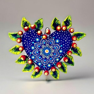 May include: A heart-shaped wall decoration, hand-painted with a deep blue base and a white dotted pattern. The centre features a mandala design. It is decorated with green and yellow leaves and red berry-like accents.