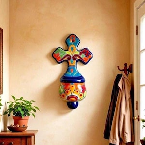 May include: A decorative ceramic wall cross in a vibrant floral design. The cross is predominantly blue, orange, and green. It is mounted on a beige wall, adding a colourful artistic touch to the room. The cross is a unique home decor item.