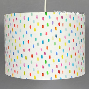 May include: A white lampshade with a repeating pattern of colourful, vertical brushstrokes in red, yellow, blue, green, and purple. The lampshade is suspended from a white cable.