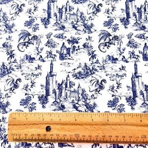 May include: White fabric with a blue toile pattern featuring castles, dragons, and figures on horseback. A wooden ruler with inch measurements is at the bottom of the image, showing approximately 8 inches.