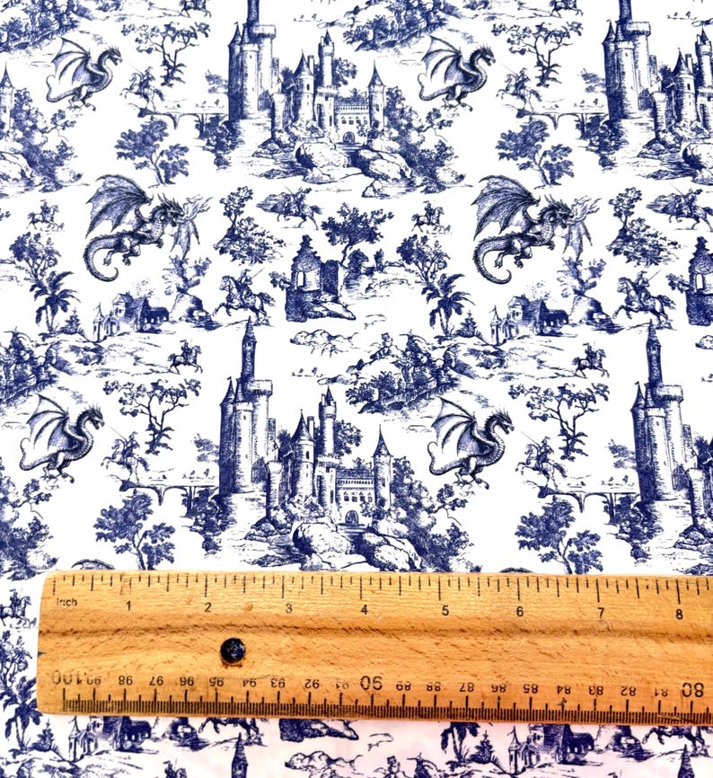 May include: White fabric with a blue toile pattern featuring castles, dragons, and figures on horseback. A wooden ruler with inch measurements is at the bottom of the image, showing approximately 8 inches.