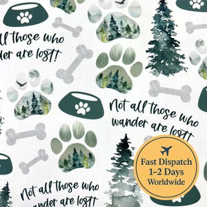 Könnte beinhalten: Weißer Stoff mit einem sich wiederholenden Muster aus Hundepfoten, Futternäpfen und Knochen in Grau- und Grüntönen. Die Pfotenabdrücke enthalten eine Aquarell-Waldszene. Der Text lautet: "Not all those who wander are lost!"