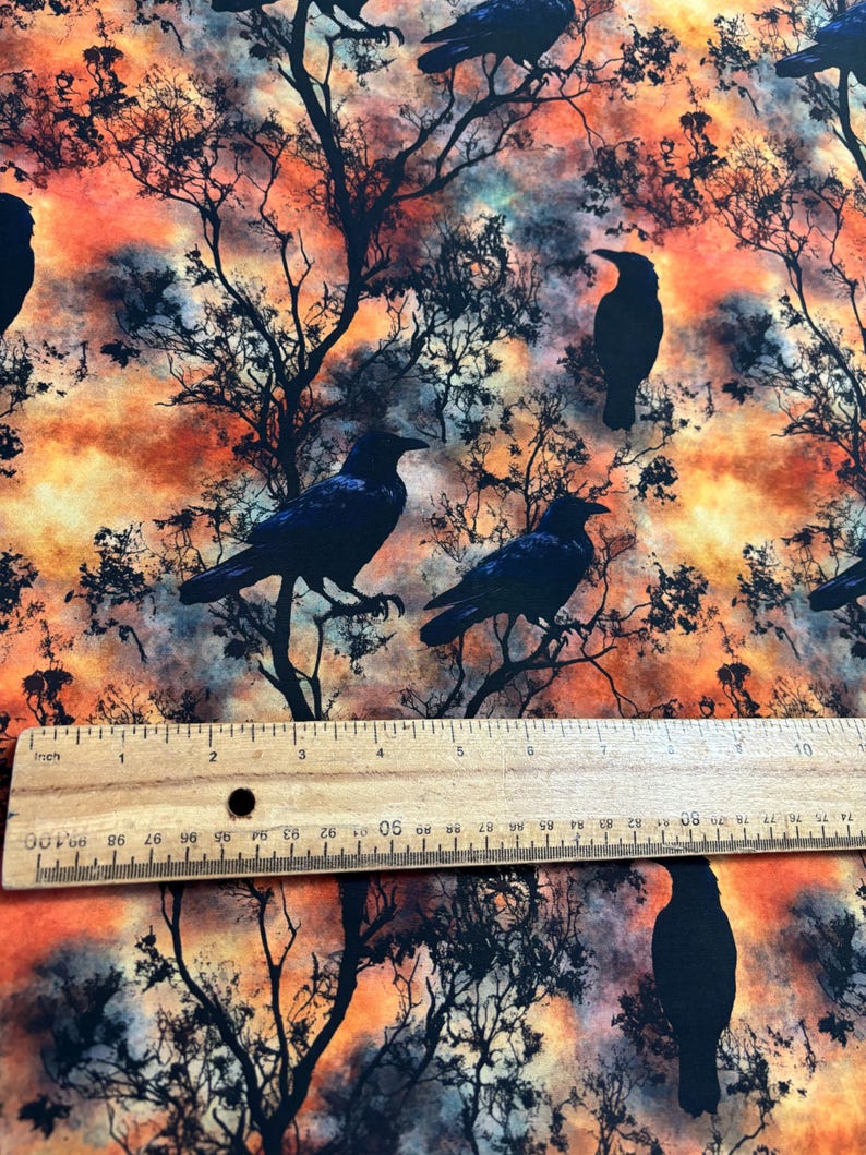 May include: A fabric with a repeating pattern of black crows silhouetted against a watercolor background of orange, yellow, and blue. The fabric has a subtle texture.