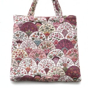 May include: A pink and white tote bag with a floral pattern. The pattern features a repeating design of pink, white, and green flowers and leaves.