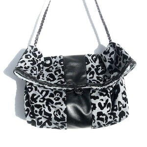 Puede incluir: Bolso de hombro con estampado de leopardo en blanco y negro, solapa de cuero negro y cadena plateada. El bolso tiene un cierre de botón y un borde superior con volantes. El bolso mide aproximadamente 25 cm de ancho y 20 cm de alto.