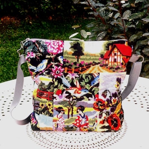 Op de afbeelding: Een schoudertas met een veelzijdig wandtapijtontwerp met diverse scènes, waaronder een huis met een rood dak, bloemmotieven en figuren in traditionele kleding. De tas is voorzien van een grijze stoffen schouderband en een ritssluiting aan de bovenkant.
