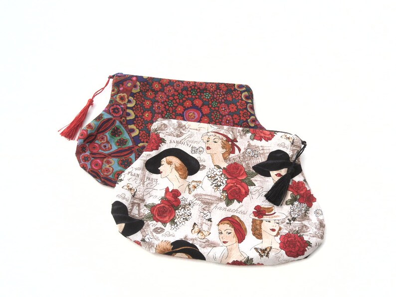 May include: Two fabric pouches with red, white, and black floral patterns. The top pouch has a red tassel. The bottom pouch has a white background with a black tassel and a repeating pattern of women wearing hats and flowers.