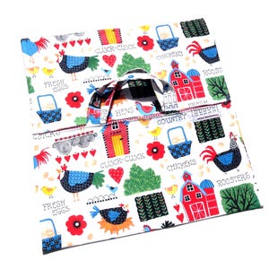 Puede incluir: Una bolsa de tela blanca con un estampado colorido de animales de granja. La bolsa presenta graneros rojos, pollos, gallos, gallinas y el texto "Fresh Eggs", "Cluck-Cluck", "Country" y "Chickens".