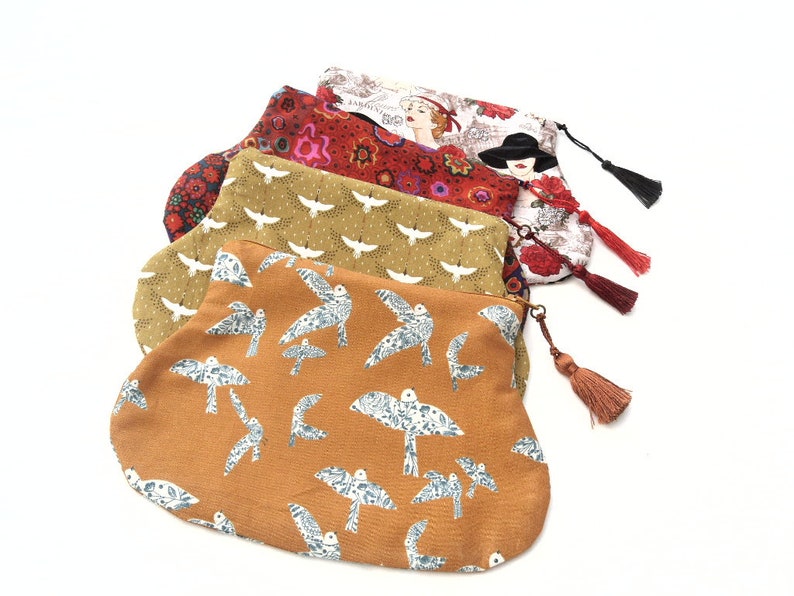 May include: Four fabric pouches with different patterns and colors. The pouches have tassels and are made of a soft, textured fabric. The patterns include birds, flowers, and geometric designs.