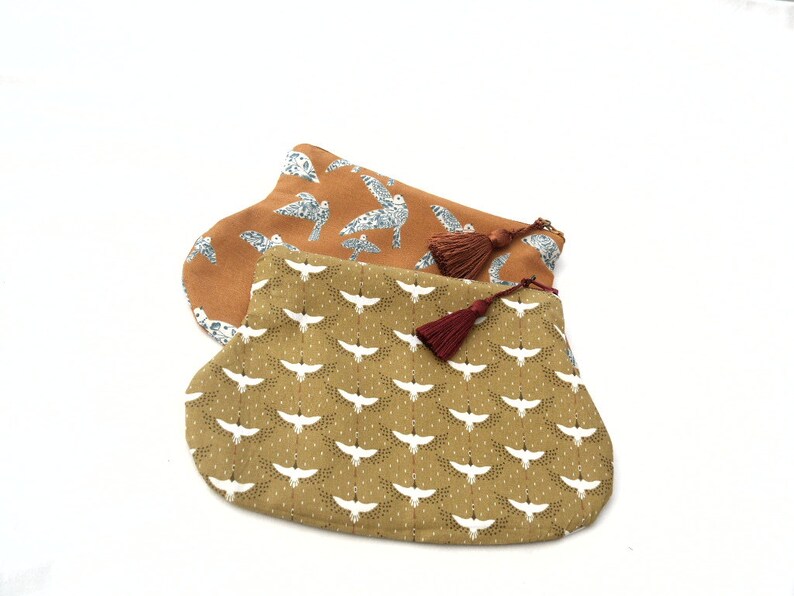 May include: Two fabric pouches with a brown and gold background and white bird patterns. Both pouches have a maroon tassel.