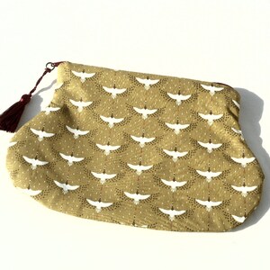 May include: A small, green pouch with a white crane pattern and a burgundy tassel. The pouch is made of fabric and has a zipper closure.