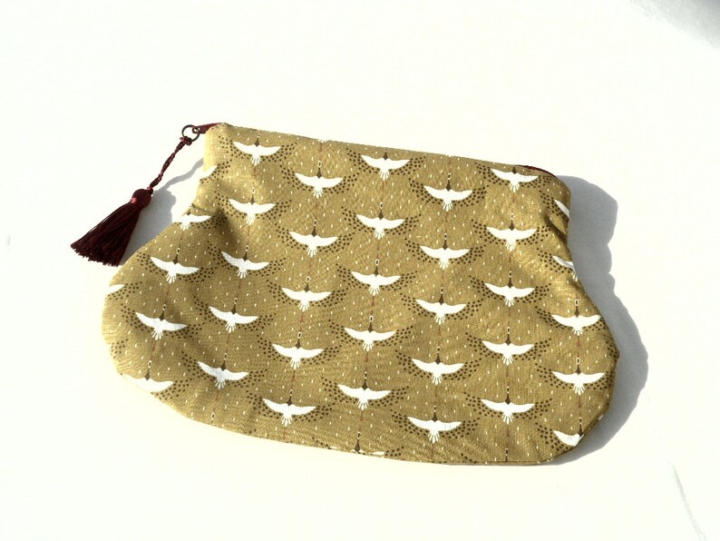 May include: A small, green pouch with a white crane pattern and a burgundy tassel. The pouch is made of fabric and has a zipper closure.