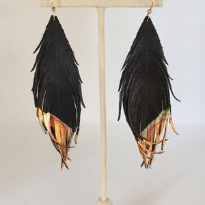 May include: Black leather fringe earrings with gold accents. The fringe is layered and the earrings are teardrop shaped.