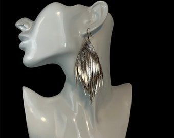 May include: Silver leather fringe earrings with a teardrop shape. The earrings are hanging from a mannequin's ear.