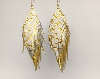 May include: White leather earrings with gold accents. The earrings are shaped like feathers and have a fringe design.